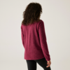 Personne aux cheveux bouclés et foncés vue de dos, portant un pull bordeaux et des leggings noirs sur un fond clair