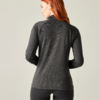 Achteraanzicht van een persoon met rood haar die een donkergrijze, gestructureerde lange mouw top en zwarte leggings draagt voor een licht, neutrale achtergrond
