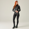 Persoon met lang rood haar staand voor een effen achtergrond, draagt een donker shirt met lange mouwen, zwarte legging en wandelschoenen, handen gevouwen voor zich, kijkt iets naar rechts