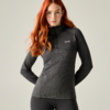 Vrouw met lang rood haar, donkergrijze sporttrui met korte rits en zwarte legging, handen achter de rug, lichte achtergrond