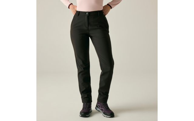 Onderlichaam en heupen van een persoon met zwarte broek en roze longsleeve, handen in de heupen, paarse wandelschoenen, lichte achtergrond