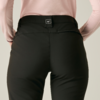 Achteraanzicht van een persoon met een zwarte broek en lichtroze longsleeve, handen op de heupen, klein vierkant label op de tailleband, effen lichte achtergrond