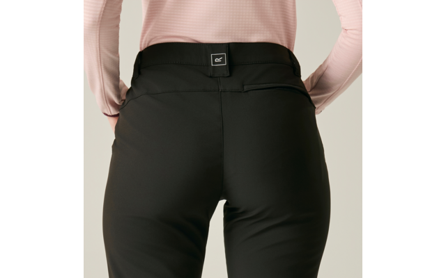 Achteraanzicht van een persoon met een zwarte broek en lichtroze longsleeve, handen op de heupen, klein vierkant label op de tailleband, effen lichte achtergrond