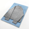 Hellgrauer Pullover mit Zopfmuster liegt auf blauem Untergrund
