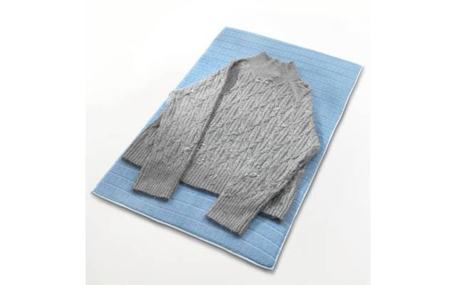 Hellgrauer Pullover mit Zopfmuster liegt auf blauem Untergrund