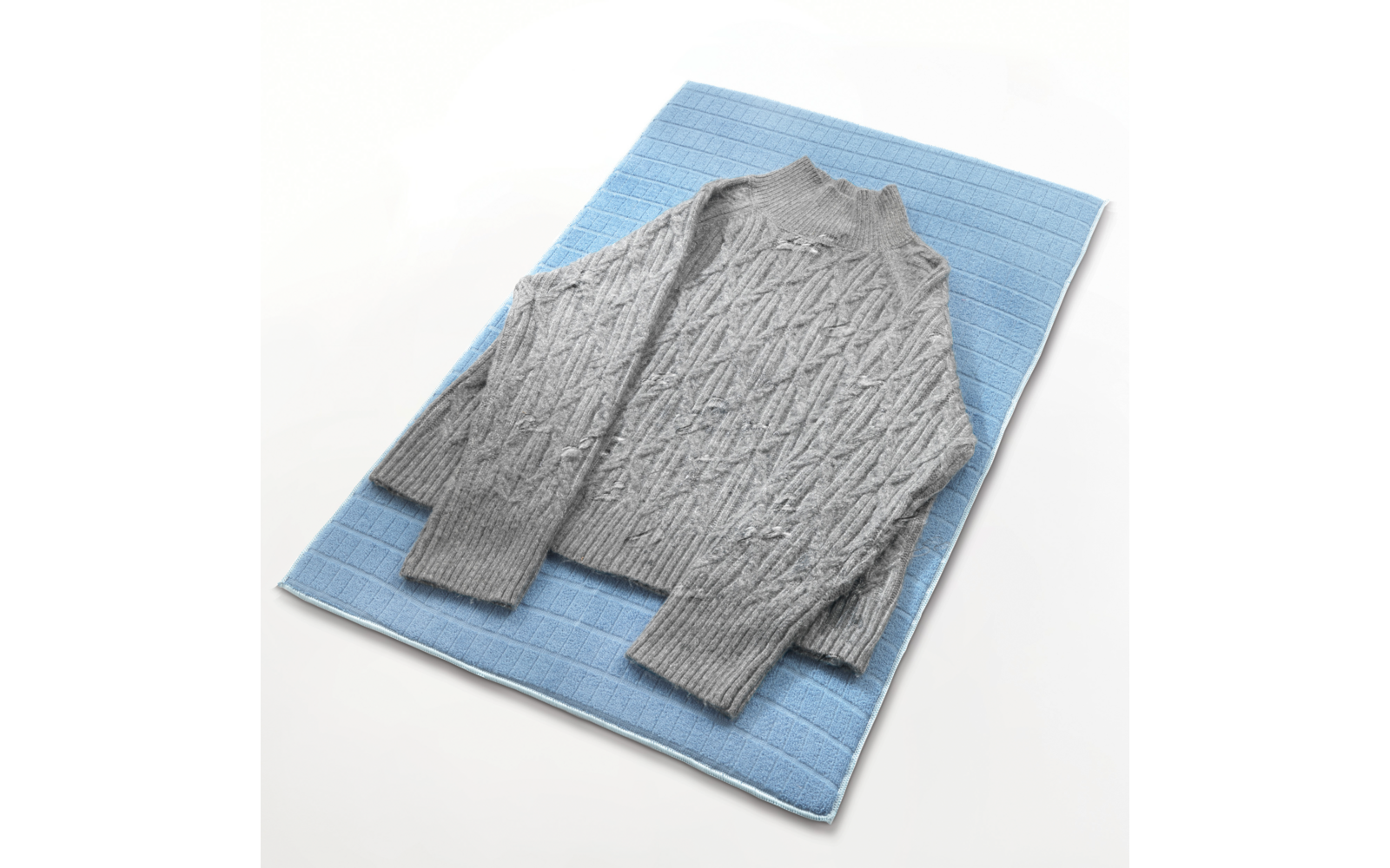 Hellgrauer Pullover mit Zopfmuster liegt auf blauem Untergrund