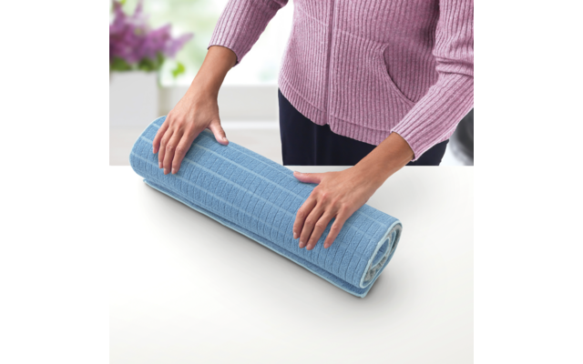 Person rollt eine blaue Yogamatte auf einem weißen Tisch zusammen