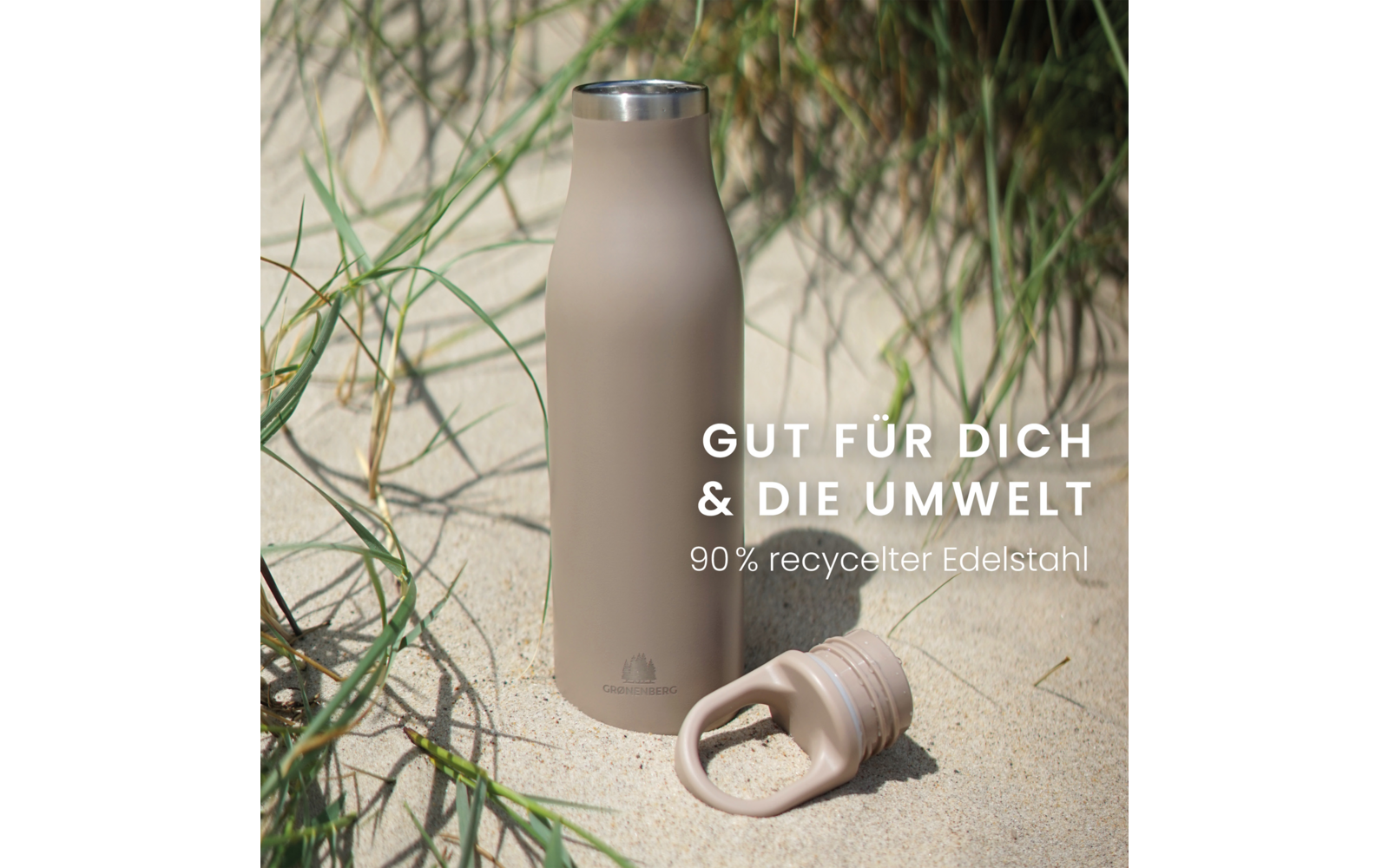Beige Edelstahl-Trinkflasche steht im Sand zwischen Dünengras, Schraubverschluss liegt daneben; weißer Text: 'GUT FÜR DICH & DIE UMWELT' und '90% recycelter Edelstahl'