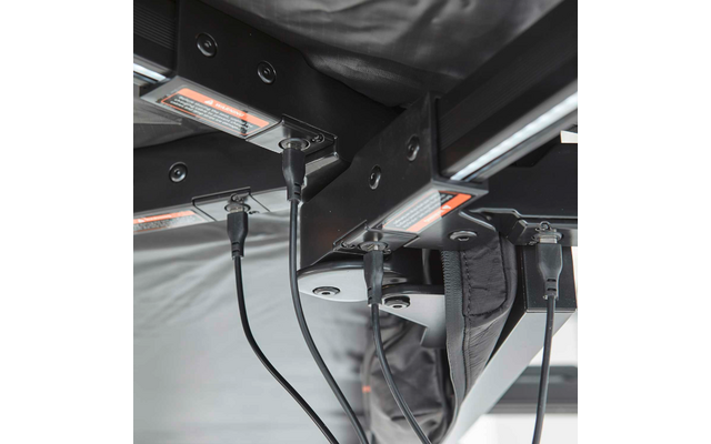 Metallrahmen von unten, mehrere schwarze Kabel an Steckverbindern, orange Warnaufkleber, grauer Stoff, sichtbare Schrauben und Halterungen