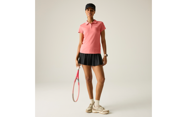 Person in rosa Poloshirt, schwarzem Tennisrock und schwarzer Kappe, hält einen Tennisschläger; trägt weiße Socken, beige Sportschuhe und eine Armbanduhr