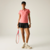 Person in rosa Poloshirt, schwarzem Tennisrock und schwarzer Kappe, hält einen Tennisschläger; trägt weiße Socken, beige Sportschuhe und eine Armbanduhr