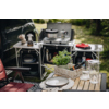 Campingküche mit Kochutensilien, Pfanne auf dem Herd und einem gedeckten Holztisch im Freien