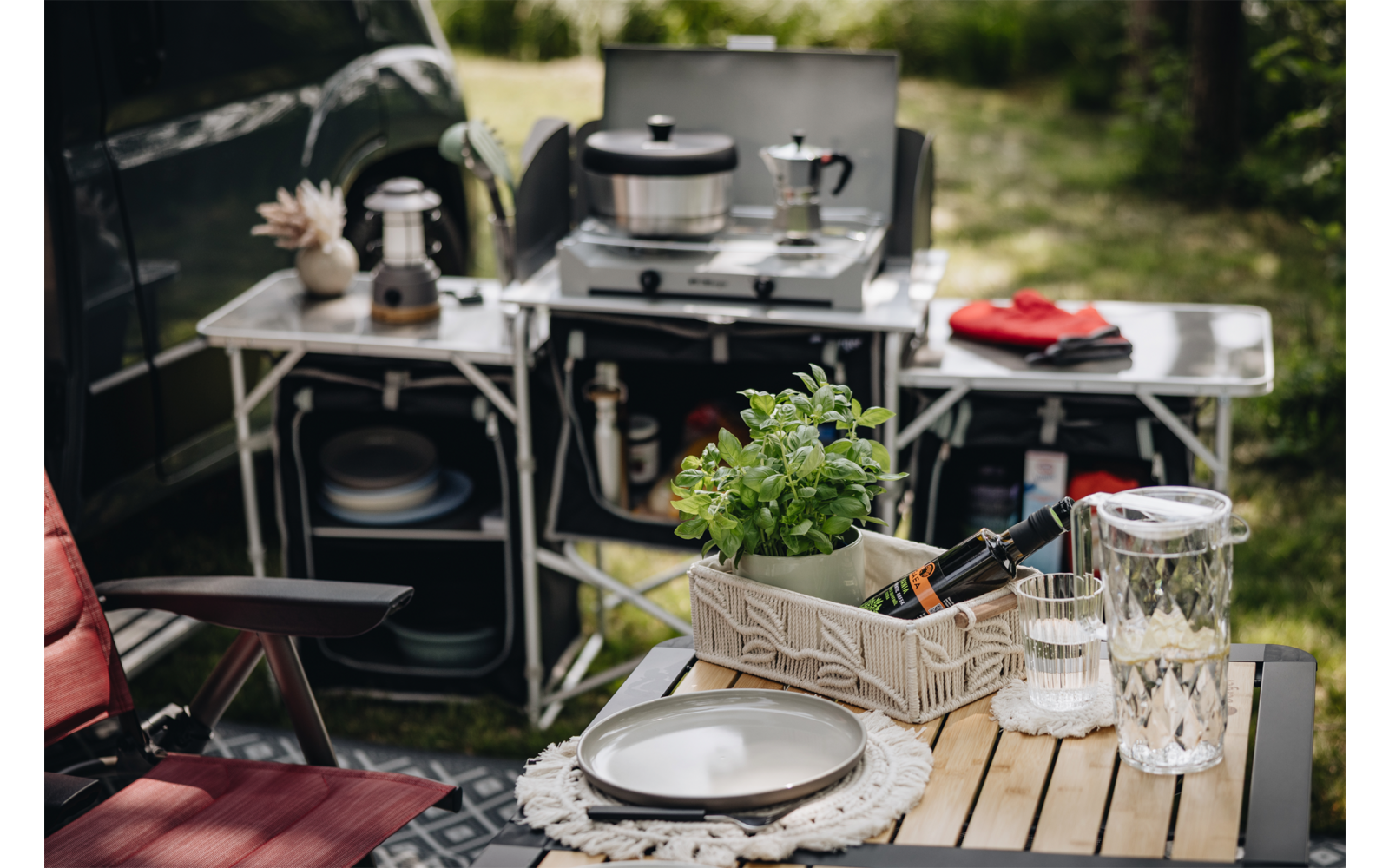 Campingküche mit Kochutensilien, Pfanne auf dem Herd und einem gedeckten Holztisch im Freien