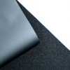 Coin replié d'un matériau gris-bleu à texture grainée sur un support noir texturé, fond blanc