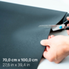 Deux mains coupant un matériau noir texturé avec des ciseaux ; en bas à gauche le texte '70,0 cm x 100,0 cm 27,6 in x 39,4 in'