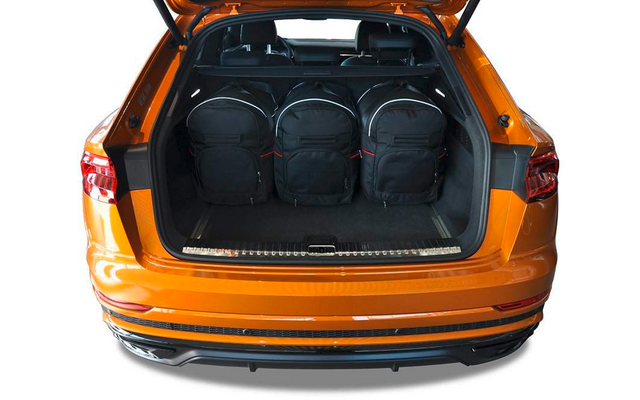 Offener Kofferraum eines orangefarbenen Autos mit drei schwarzen Rucksäcken, Rücksitze und Kopfstützen sichtbar