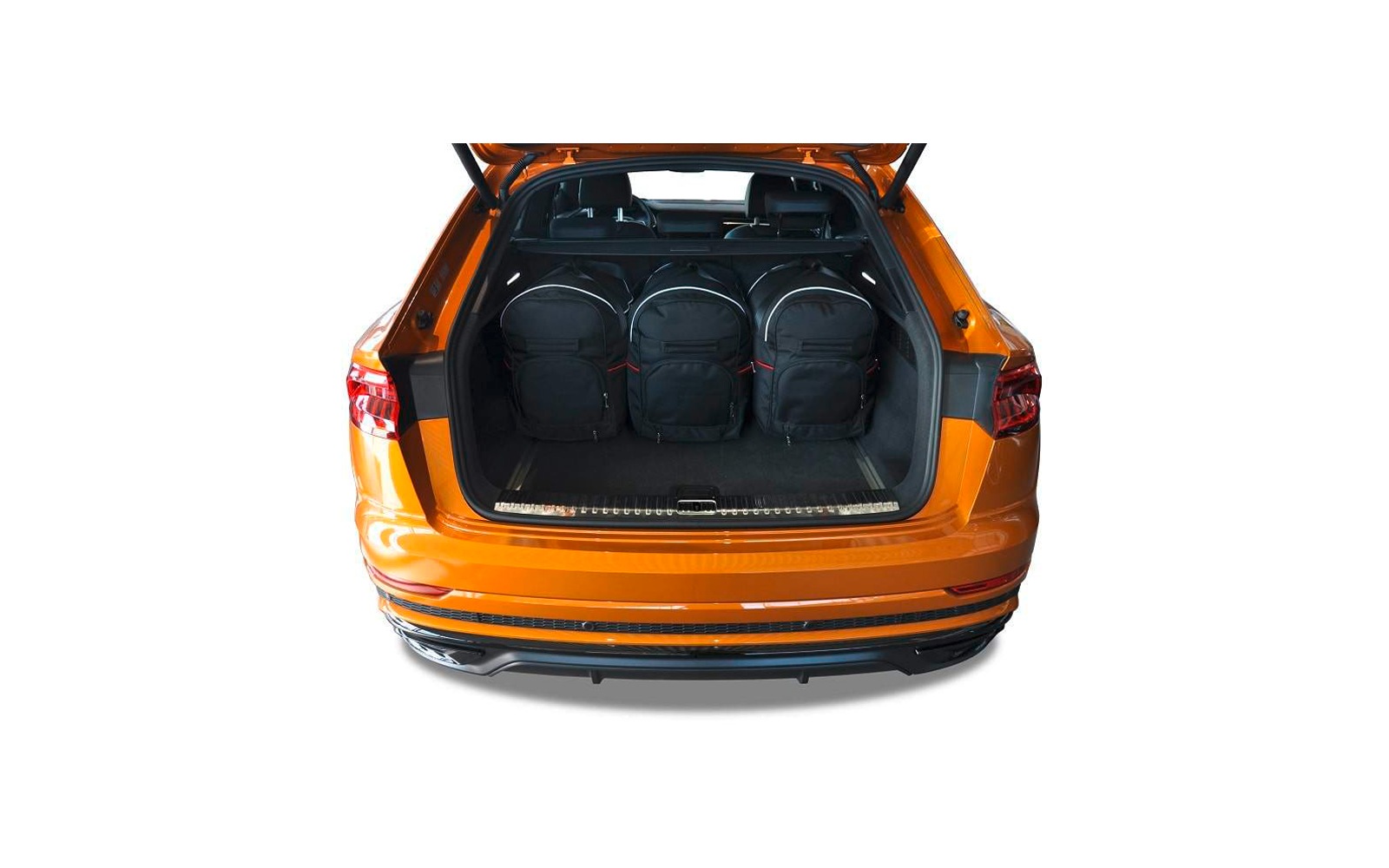 Offener Kofferraum eines orangefarbenen Autos mit drei schwarzen Rucksäcken, Rücksitze und Kopfstützen sichtbar