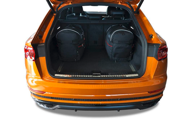 Geöffneter Kofferraum eines orangefarbenen Autos mit zwei schwarzen Rucksäcken im Innenraum