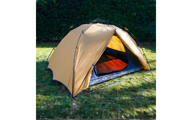 Beiges Zelt auf Rasen, geöffneter Eingang mit sichtbarem roten Schlafsack auf blauer Isomatte; Hecke im Hintergrund