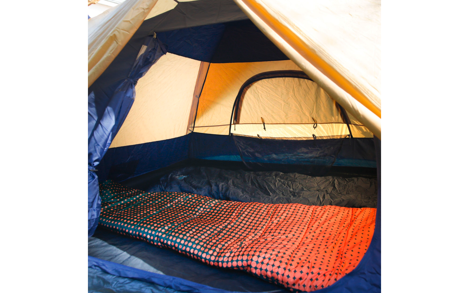 Innenraum eines Zelts mit geöffnetem Eingang, blauen Innenwänden, orange-rot gemustertem Textil auf dem Zeltboden und sichtbarem Netzfenster