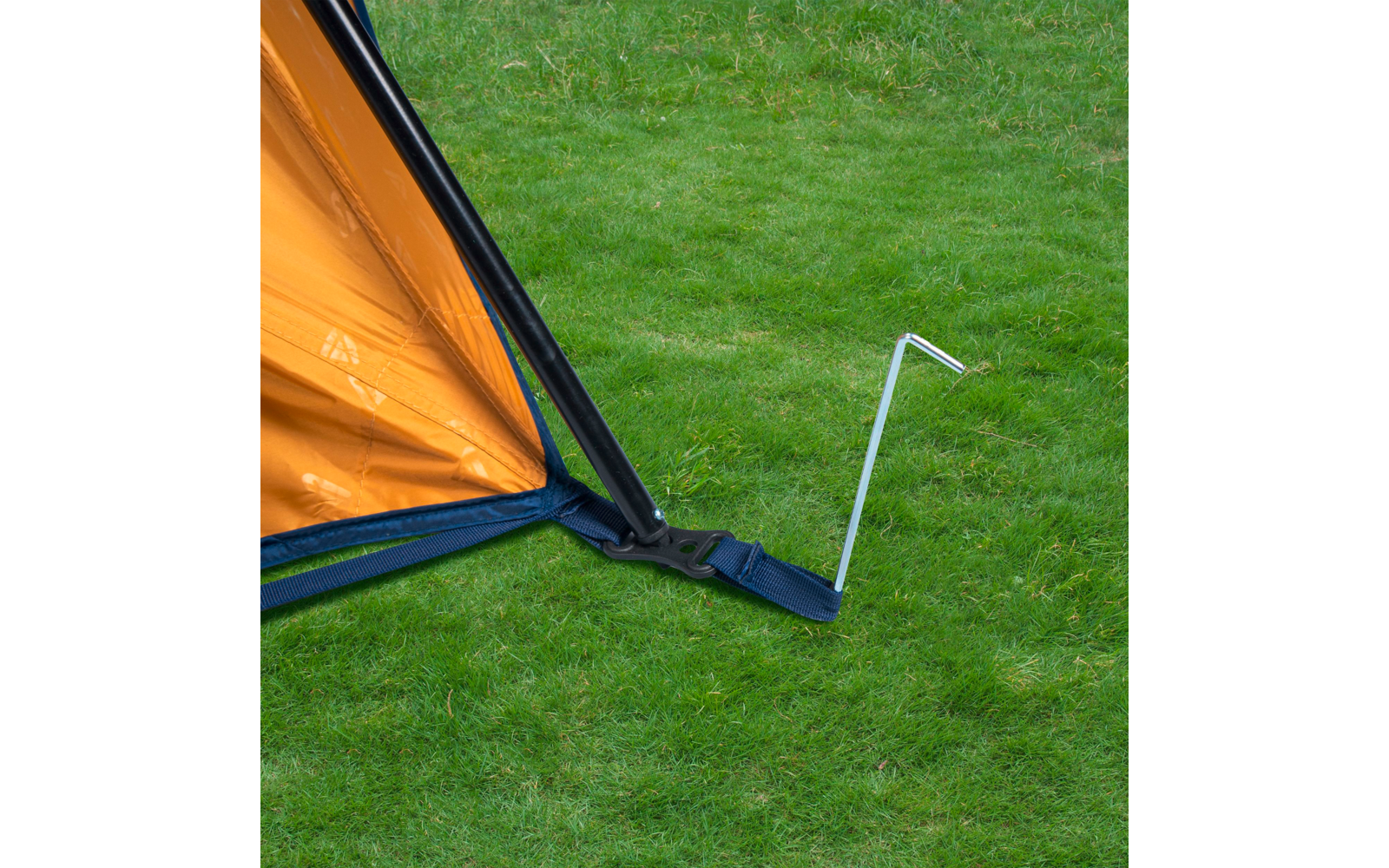 Ecke eines orangefarbenen Zeltes mit schwarzem Gestänge, blauem Spannriemen und einem in grünen Rasen eingeschlagenen Metallhering