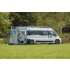 Witte camper met een grijs zijluifel bevestigd aan de zijkant op een grasveld, bomen en riet op de achtergrond