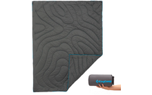 Eine gefaltete graue Campingdecke mit einer hellblauen Umrandung neben einer aufgerollten dunkelblauen Tasche