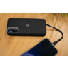 Schwarze Powerbank mit digitaler Anzeige "93%" und Aufschrift "FAST CHARGING" auf einer Holzoberfläche, per Kabel mit einem Smartphone verbunden