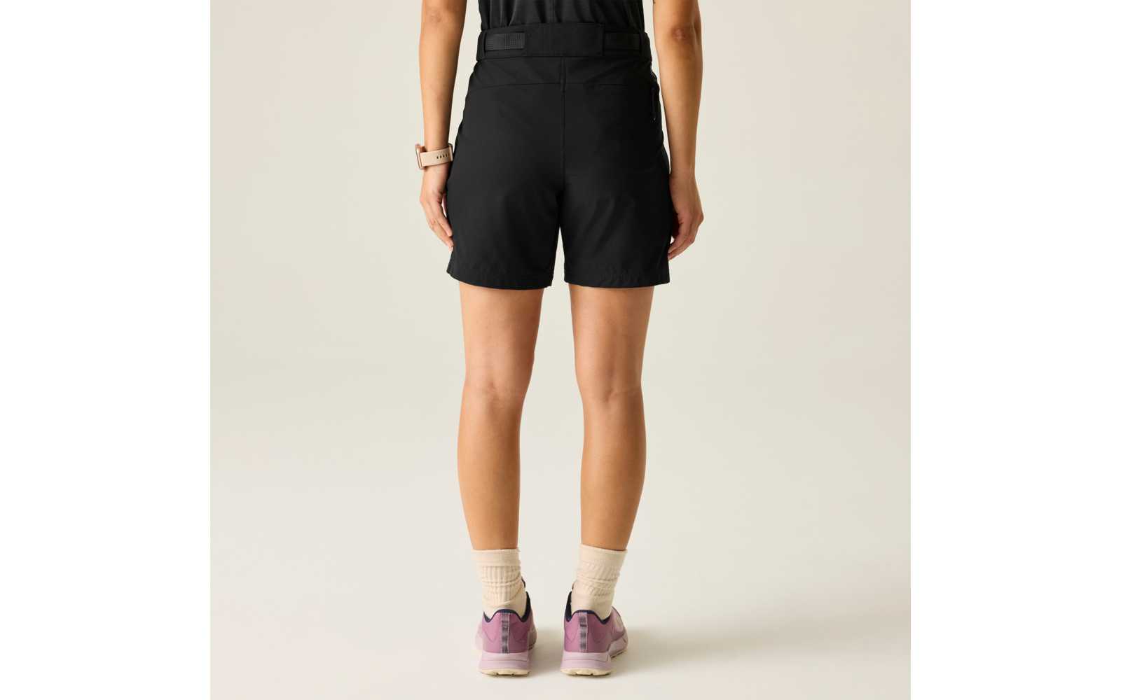 Vista posterior de una persona con pantalones cortos negros, calcetines cortos claros y zapatillas rosas sobre un fondo claro