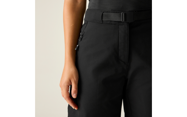 Antebrazo derecho y mano junto a pantalones negros con cinturón y bolsillos laterales con cremallera sobre fondo claro