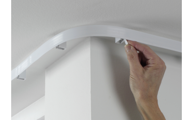 Hand befestigt eine weiße Abdeckleiste an der Decke über einer Ecke