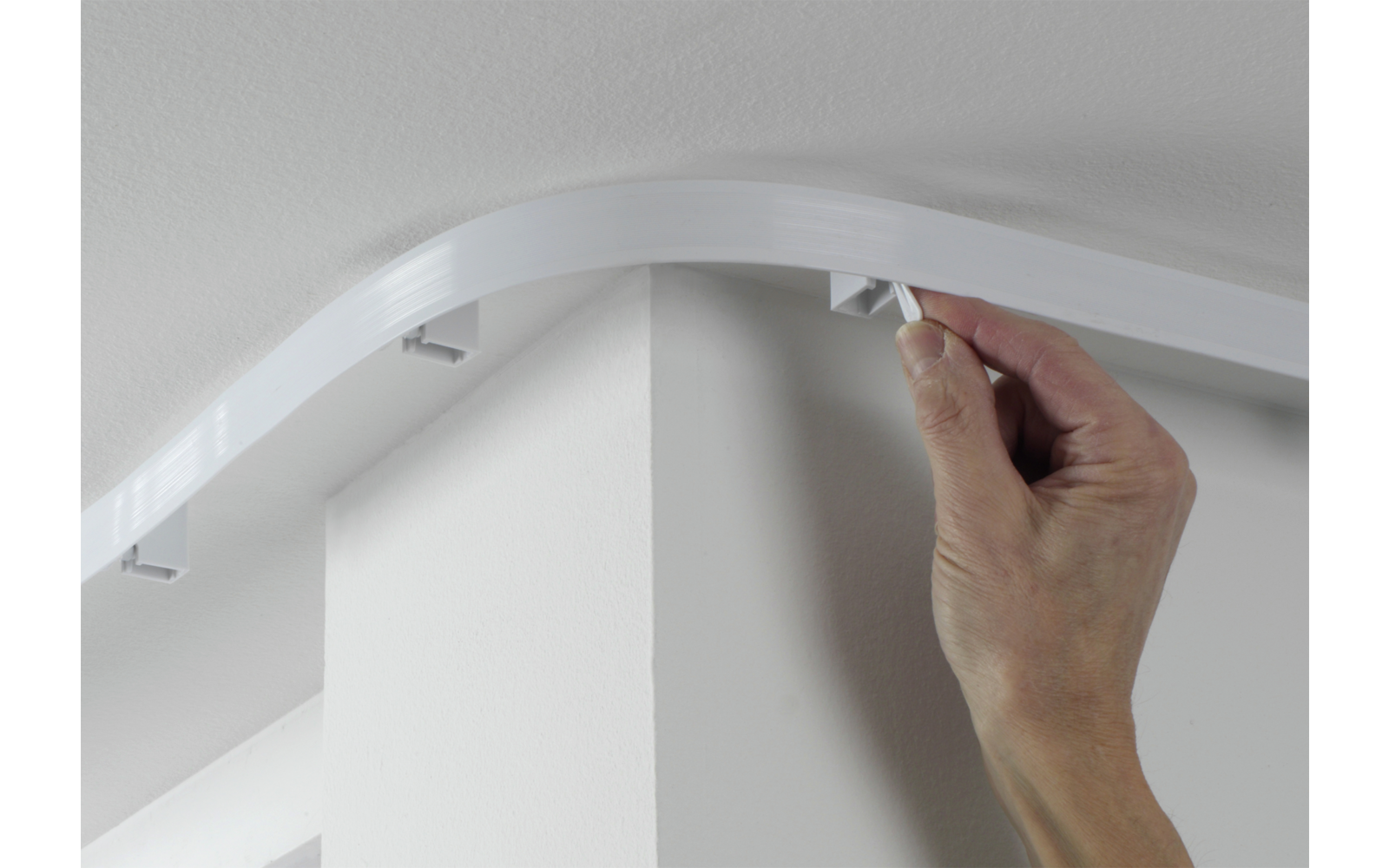 Hand befestigt eine weiße Abdeckleiste an der Decke über einer Ecke