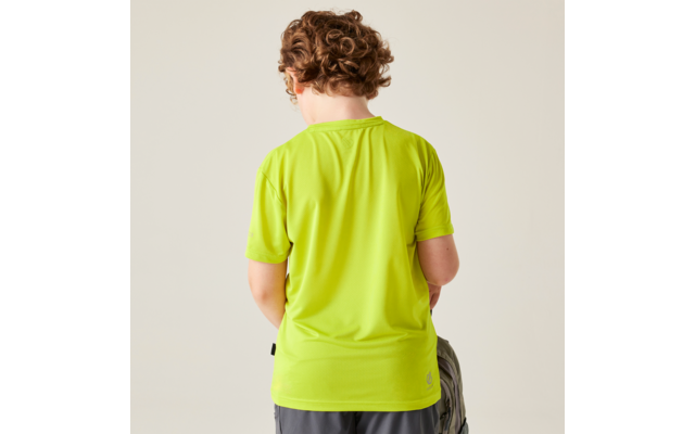 Person von hinten mit lockigen Haaren, trägt leuchtend grünes T-Shirt und graue Shorts, hält einen Rucksack, heller Hintergrund