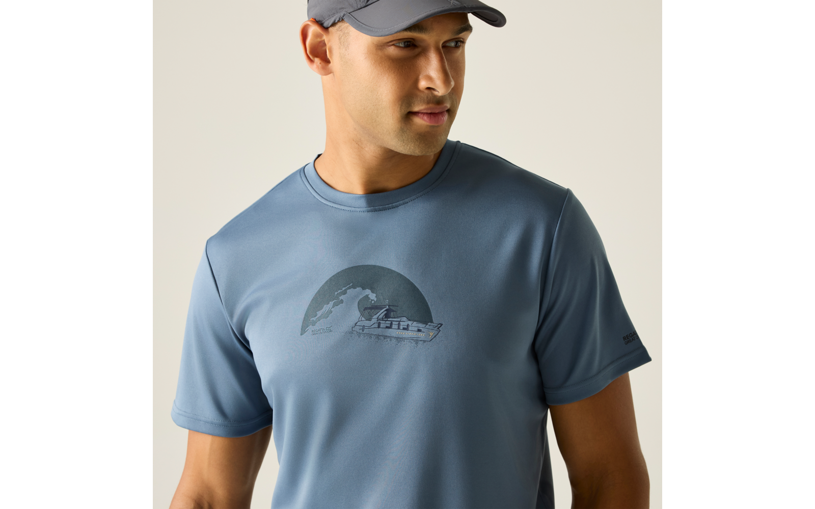 Mann mit dunkelblauer Kappe trägt blaues kurzärmeliges T-Shirt mit rundem Druck einer Welle und eines Bootes, Blick nach rechts