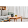 Graues Sofa, hölzerner Couchtisch mit rundem digitalen Display, auf dem '05:53' steht, kleine Schale mit grünen Blättern, Stehlampe, Regal mit Gläsern und Büchern, weiße transparente Vorhänge