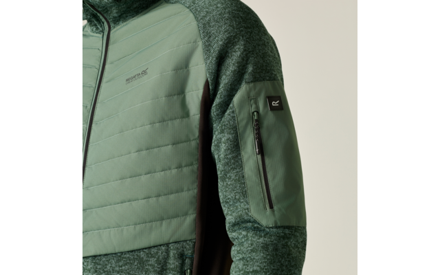 Nahaufnahme einer grünen Jacke mit gesteppter Vorderpartie, meliertem Strickärmel, Reißverschlusstasche am Oberarm und schwarzem Markenetikett