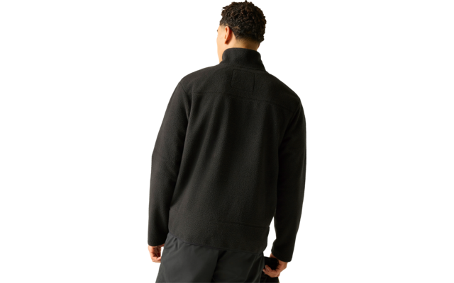 Person von hinten, trägt schwarze Fleecejacke mit Stehkragen und dunkle Hose vor hellem Hintergrund