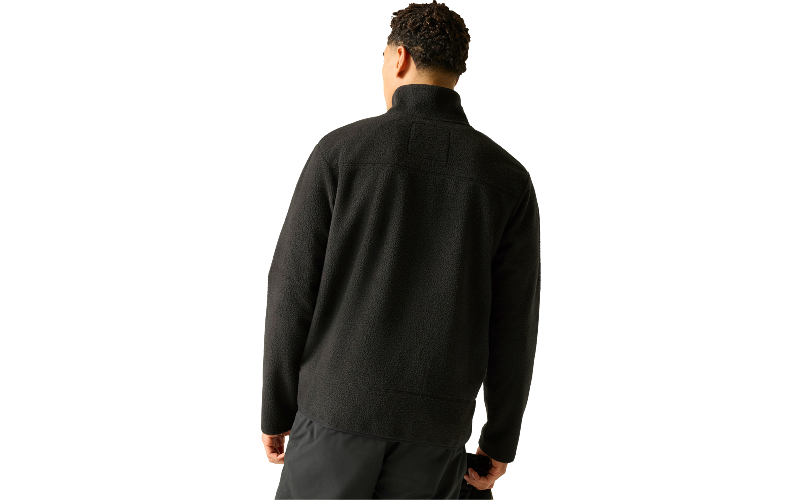 Person von hinten, trägt schwarze Fleecejacke mit Stehkragen und dunkle Hose vor hellem Hintergrund