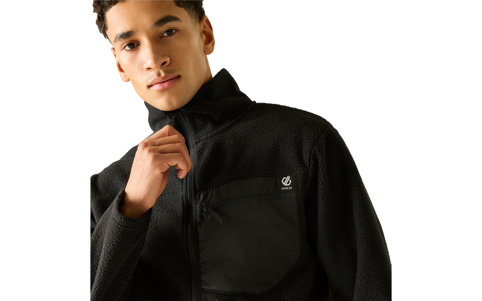 Person trägt schwarze Fleecejacke mit Reißverschluss und Brusttasche mit kleinem weißem Logo, eine Hand hält den Reißverschluss, beiger Hintergrund