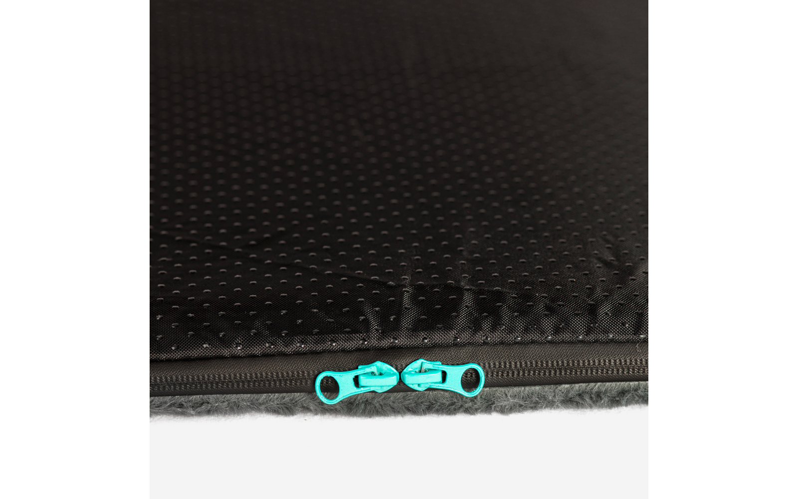 Nahaufnahme eines schwarzen, gepunkteten Stoffs mit einem geschlossenen Reißverschluss und zwei türkisen Zippern, unterer Rand zeigt graues Fell