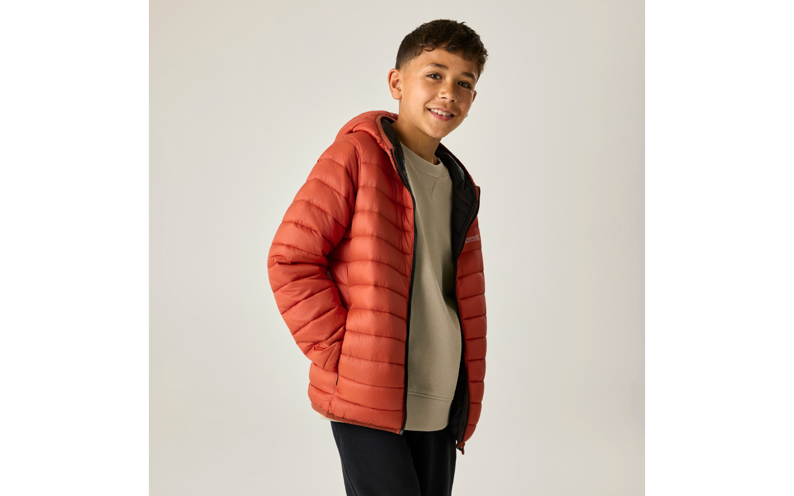 Junge in orangefarbener Steppjacke, Hände in den Taschen, lächelnd