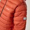 Nahaufnahme einer orangefarbenen Steppjacke mit horizontalen Steppnähten, sichtbarem schwarzen Reißverschluss, weißer Schrift "Regatta Great Outdoors" auf der Brust und rechteckigem Stoffpatch am Ärmel vor beigem Hintergrund