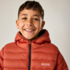 Lächelnder Junge mit Sommersprossen, trägt orangefarbene Steppjacke mit Logo