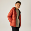 Junge in orangefarbener Steppjacke, Hände in den Taschen, lächelnd
