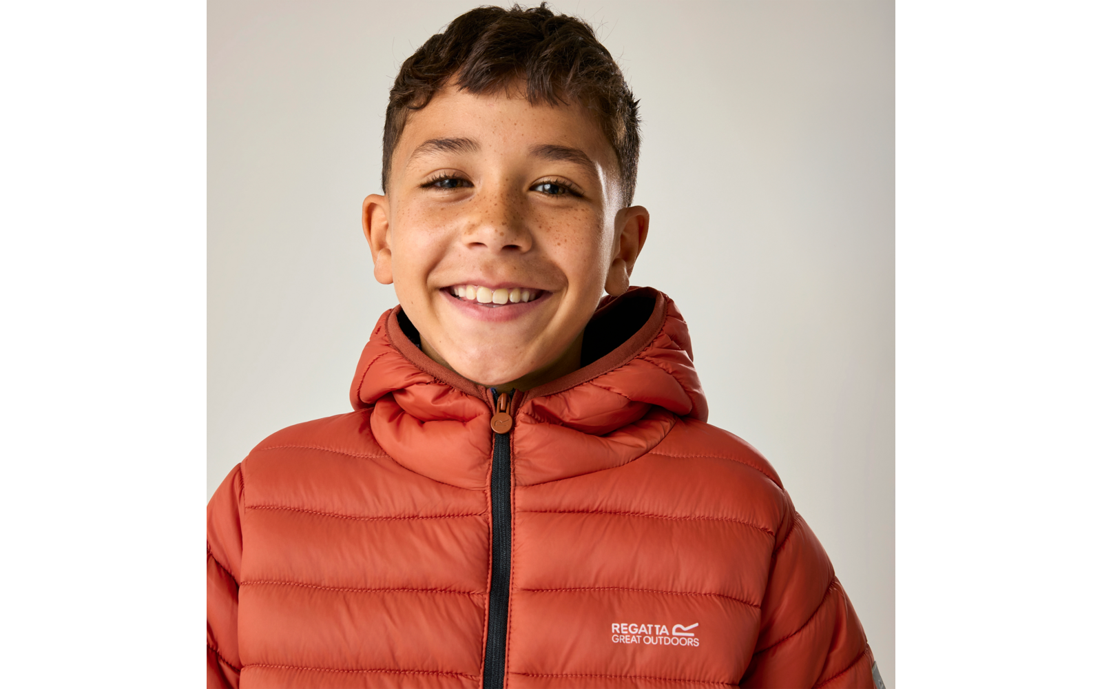 Lächelnder Junge mit Sommersprossen, trägt orangefarbene Steppjacke mit Logo