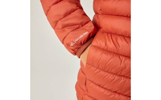 Nahaufnahme einer orangefarbenen Steppjacke (Ärmel und Oberkörper), rechte Hand in Tasche, weiße Aufschrift FEATHER FREE auf dem Ärmel, heller Hintergrund