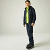 Ein Junge steht vor hellem Hintergrund, trägt eine dunkelblaue Kapuzenjacke, ein neongrünes Zip-up darunter, dunkelblaue Hose und schwarze Sportschuhe