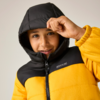 Kind in gelber und schwarzer Steppjacke mit Kapuze, Hand an der Kapuze, heller einfarbiger Hintergrund