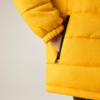 Hand in Reißverschlusstasche einer gelben Steppjacke, sichtbarer Ärmel und Saum vor hellem Hintergrund