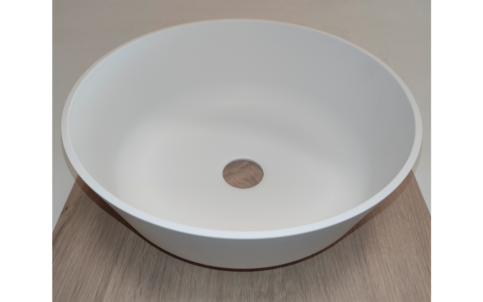 Witte ronde wastafel met centrale ronde afvoeropening op een houten oppervlak